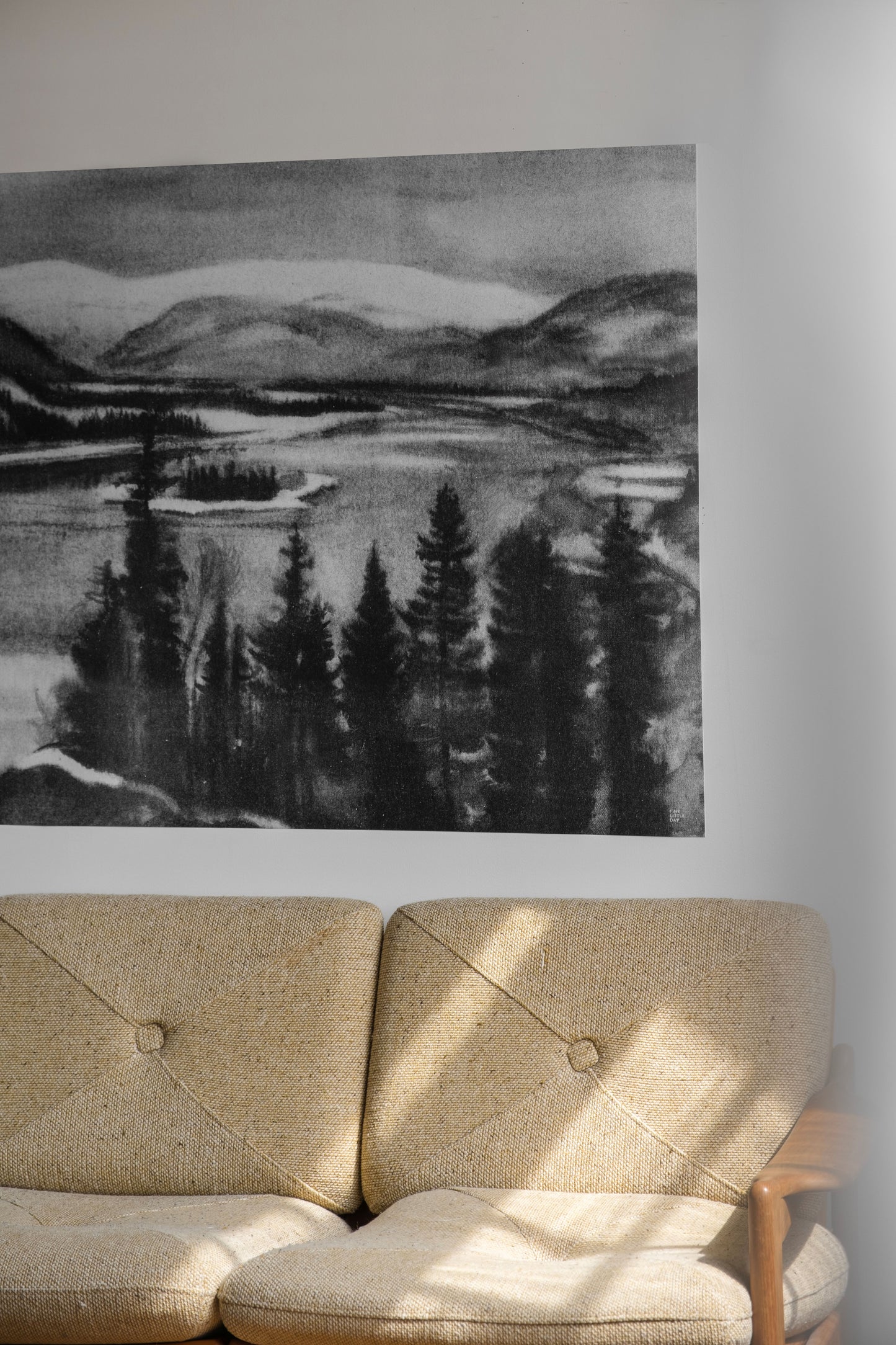 Beige sofa in front of a black and white landscape drawing on a wall.