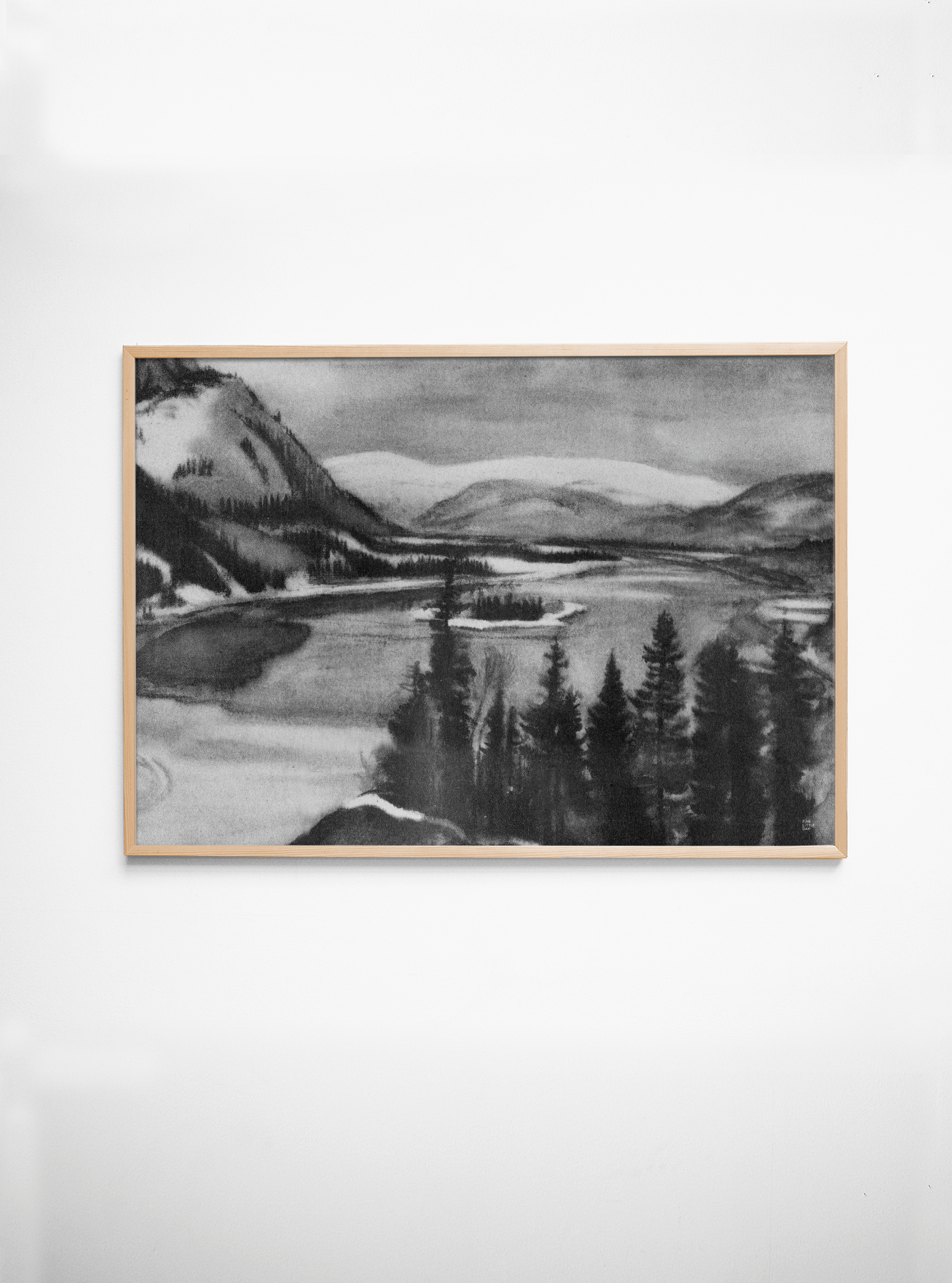Framed black and white landscape painting of a lake and mountains on a white wall.