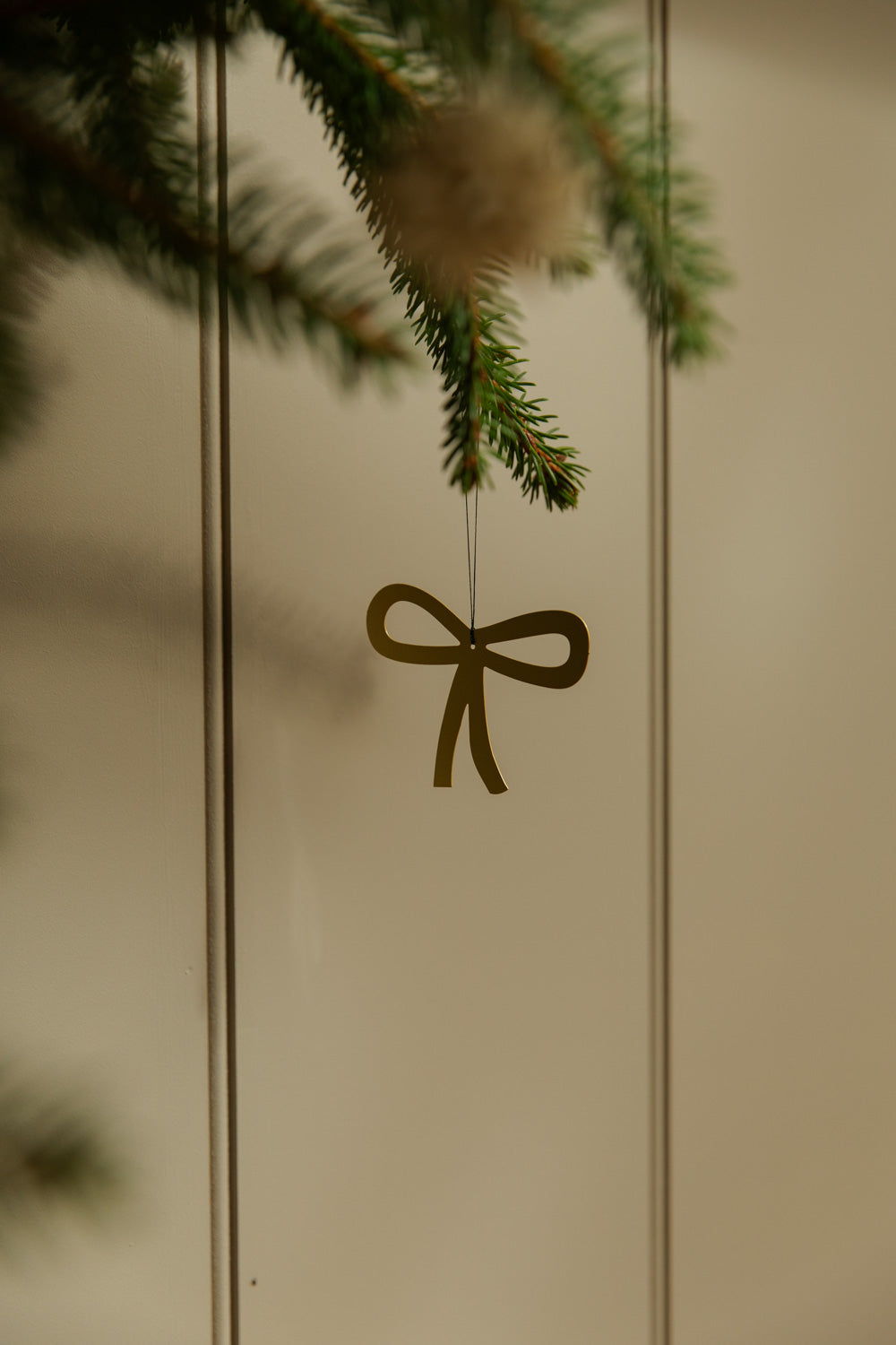 Decorative bow hanging from a branch against a neutral background.