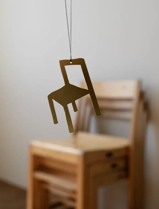 Gold chair ornament shown in front of a blurred background displaying chairs.