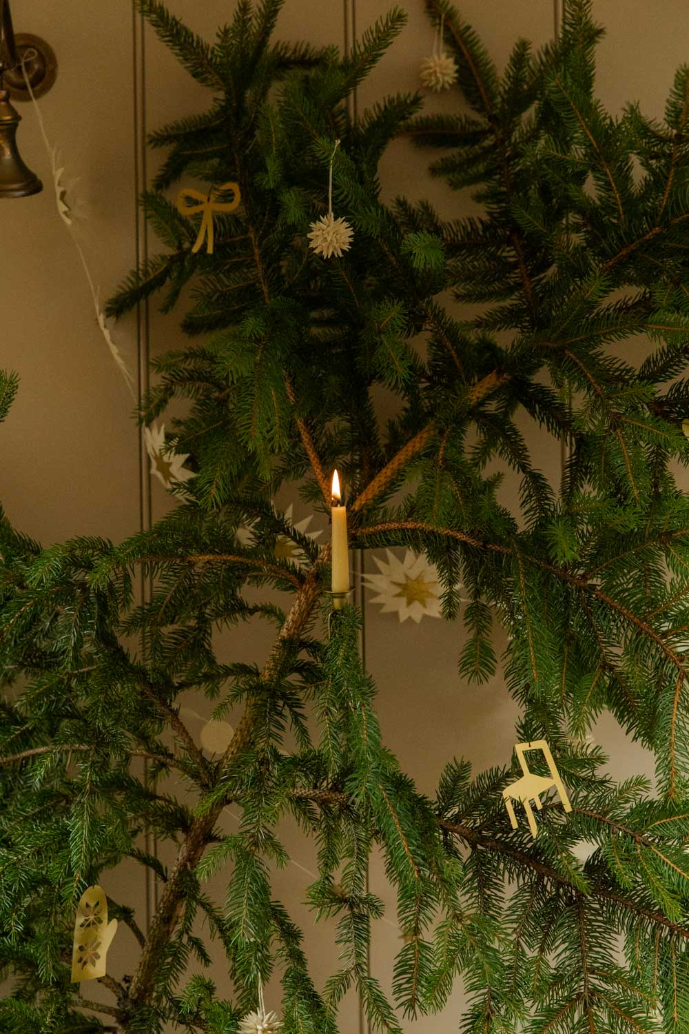 Decorative Christmas tree with candles and ornaments in front of a plain wall.