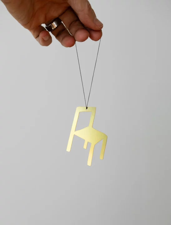 A gold-colored stainless steel chair-shaped ornament is held up against a white background, demonstrating its suspended state as a decoration.