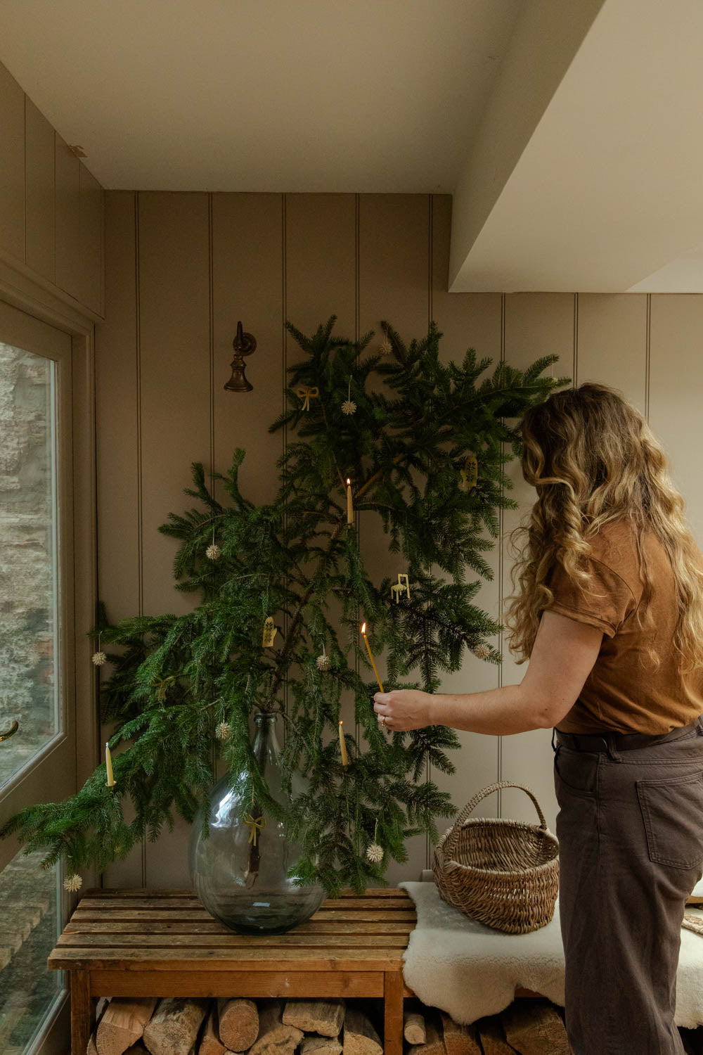 Person arranging a large green wreath in a room with wooden walls and a window.