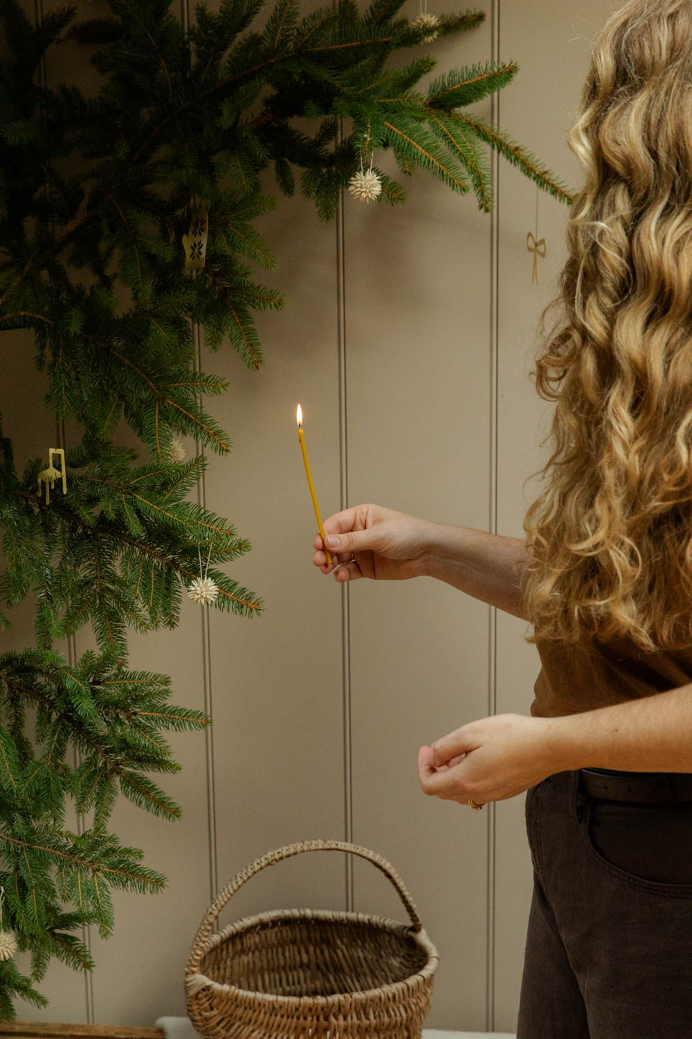 Person lighting a candle next to a decorated Christmas tree with a neutral background.