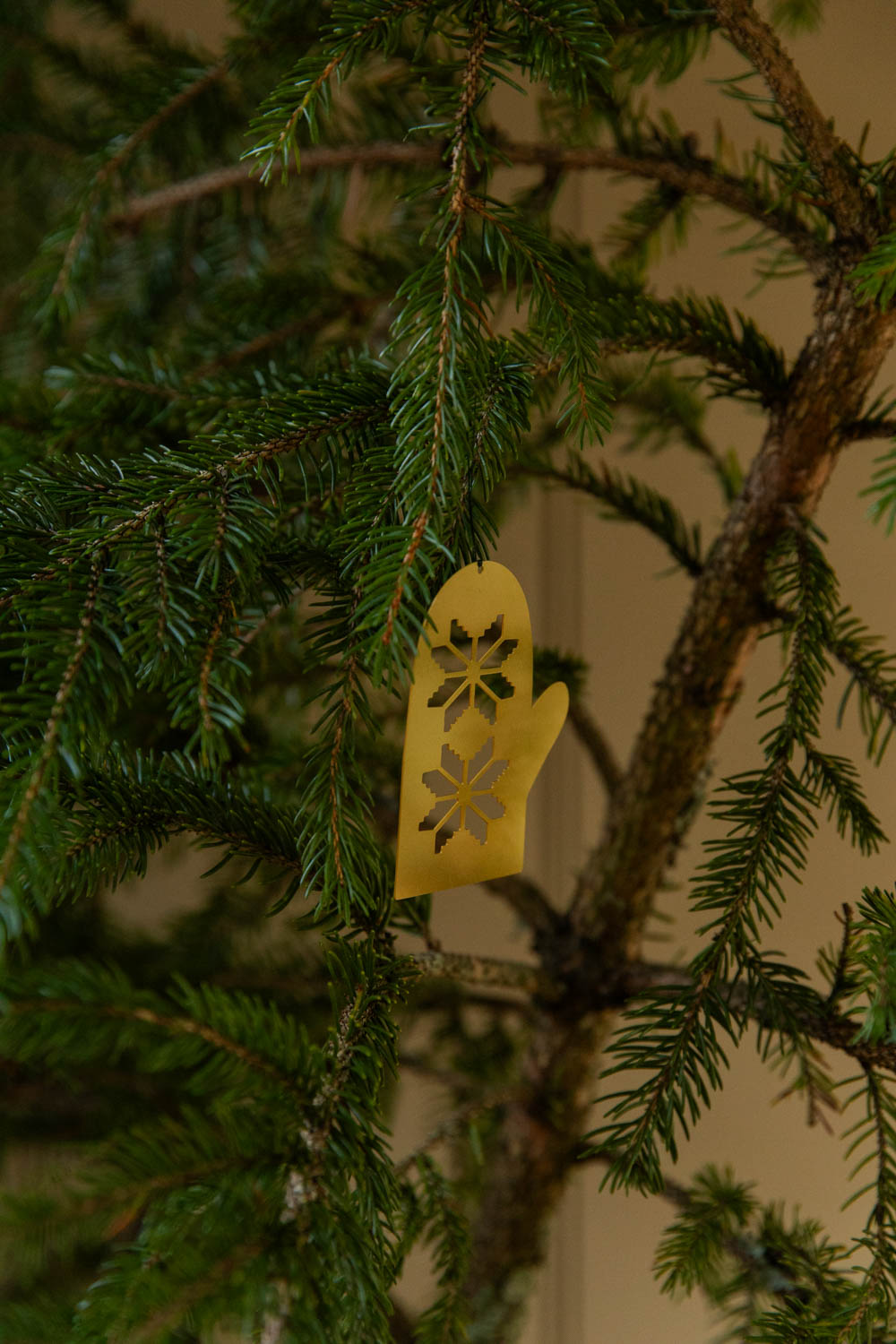 Gold decorative glove ornament on a green Christmas tree branch.