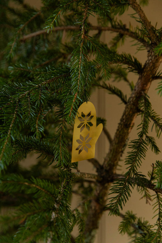 Gold decorative glove ornament on a green Christmas tree branch.