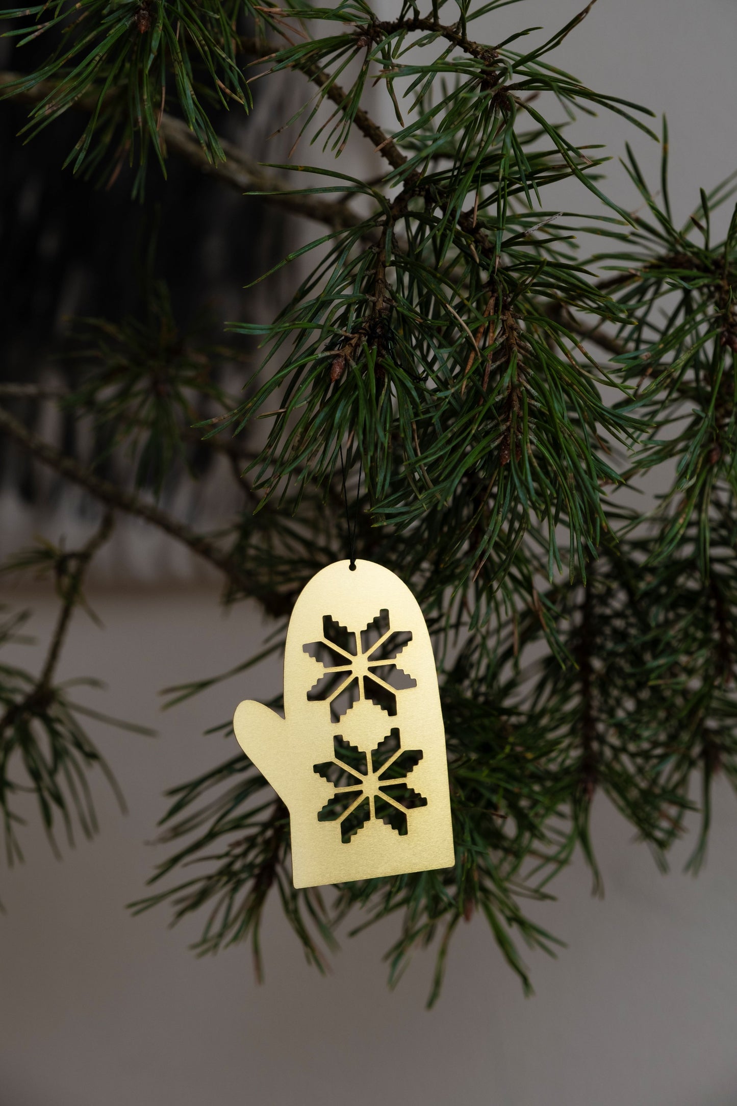 A gold-plated, stainless steel glove-shaped ornament hanging from a Christmas tree branch with green pine needles.
