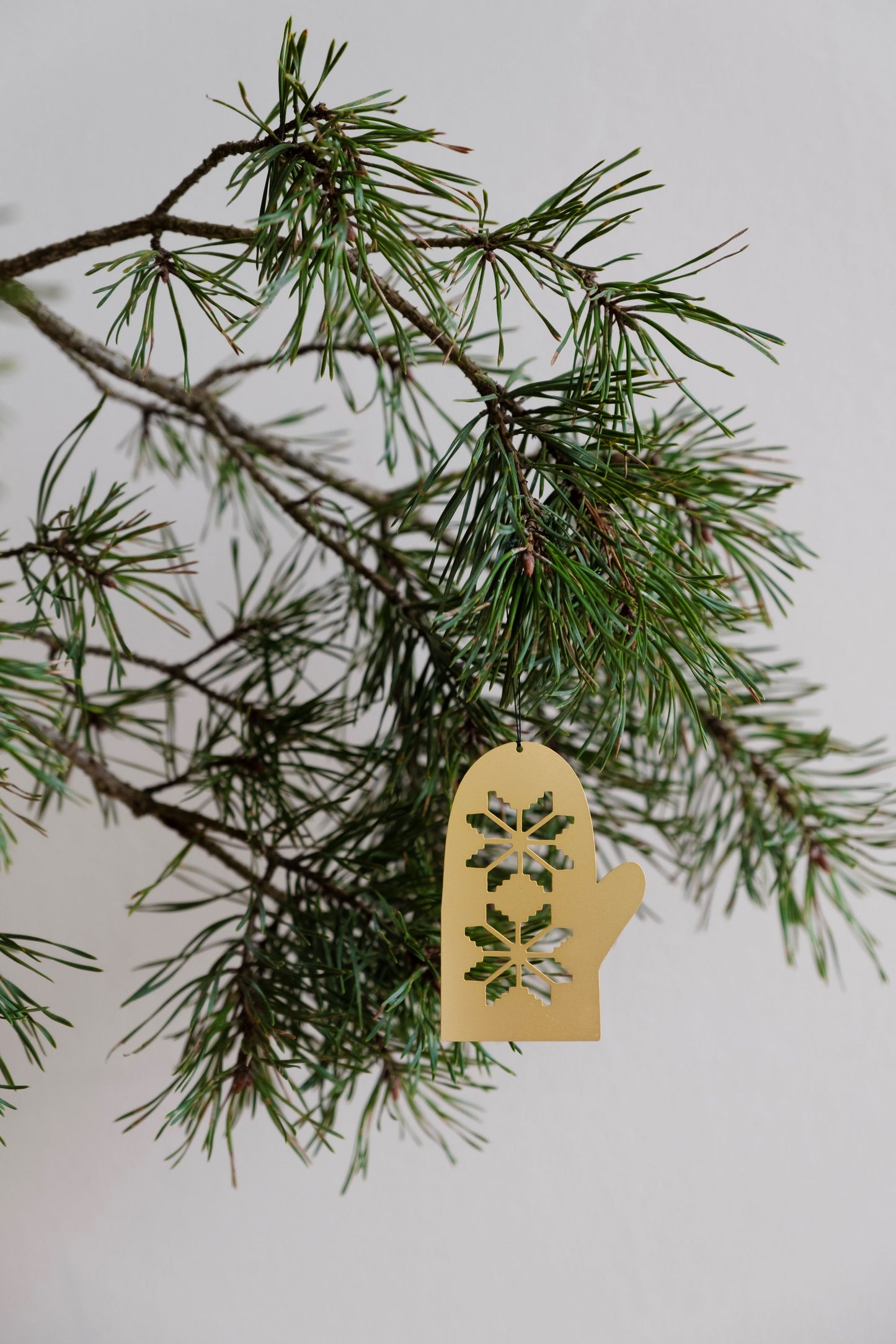 A gold-plated, stainless steel glove-shaped ornament hanging from a Christmas tree branch with green pine needles.