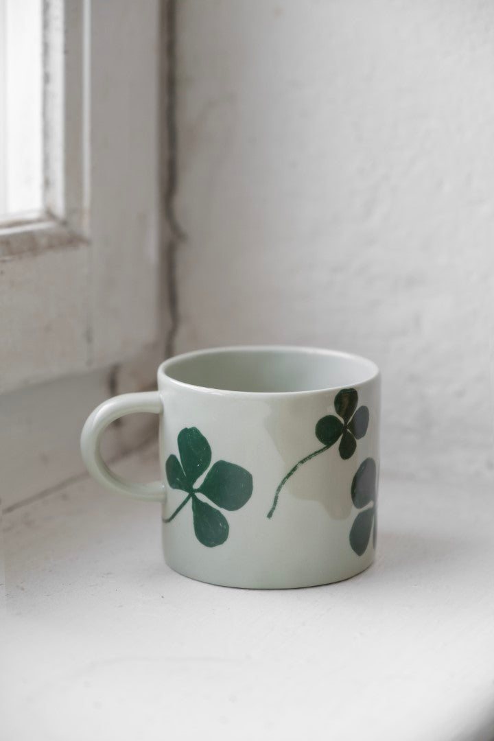 Light green porcelain cup with a green clover patten on a white windowsill.
