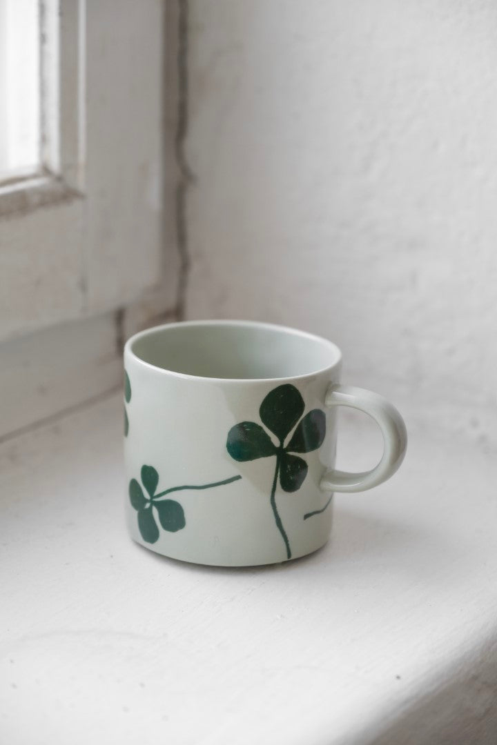 Light green porcelain cup with a green clover patten on a white windowsill.