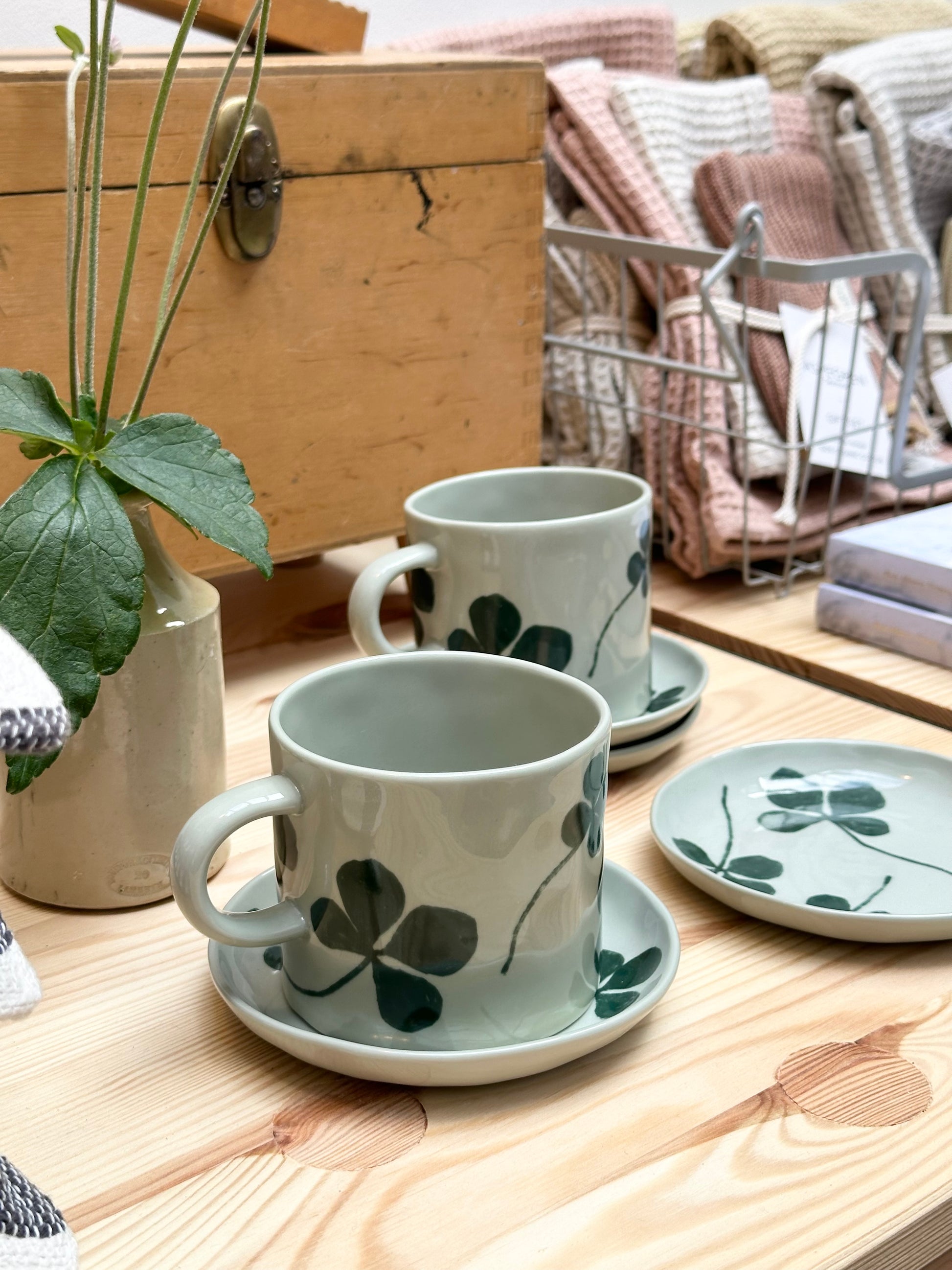 Gathering of porcelain clover cups and lates next to a wooden box and plant.