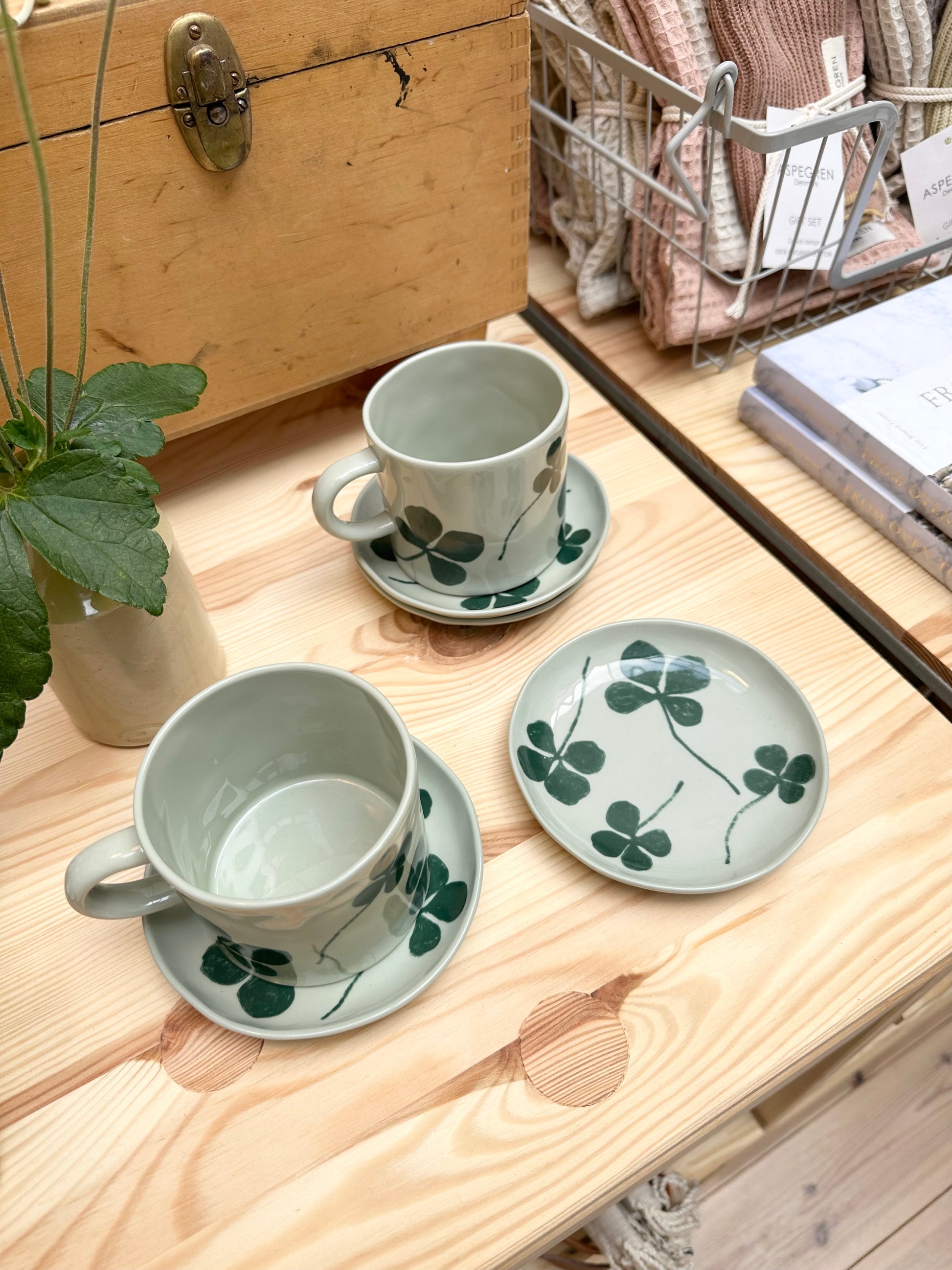 Gathering of porcelain clover cups and lates next to a wooden box and plant.