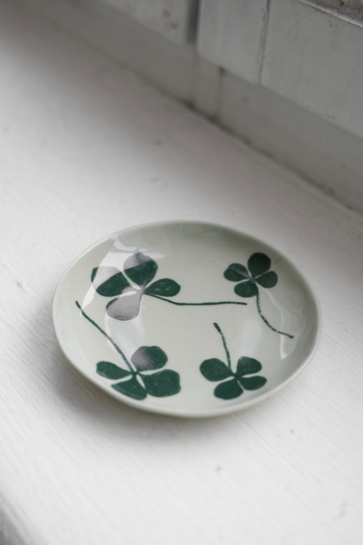A round porcelain plate with a green four-leaf clover design, placed on a white surface.