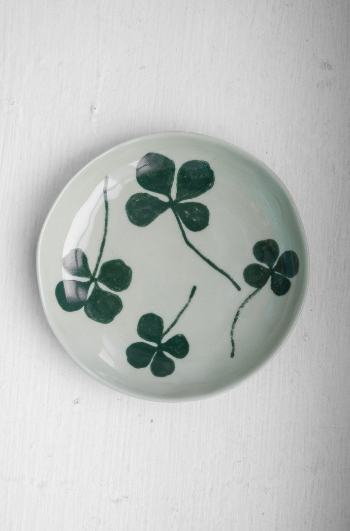 A round porcelain plate with a green four-leaf clover design, placed on a white surface.