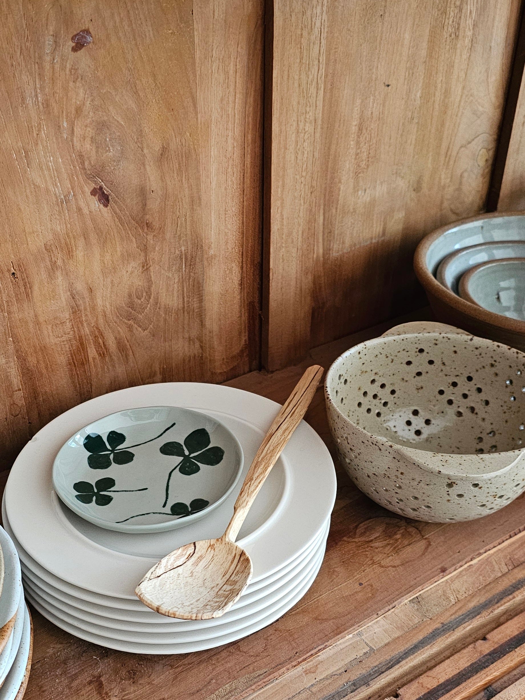 A round porcelain plate with a green four-leaf clover design, placed on a wooden surface amongst other dinnerware.