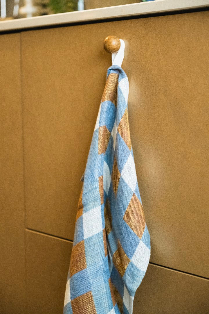 A checkered linen tea towel hanging on a wooden cabinet handle.