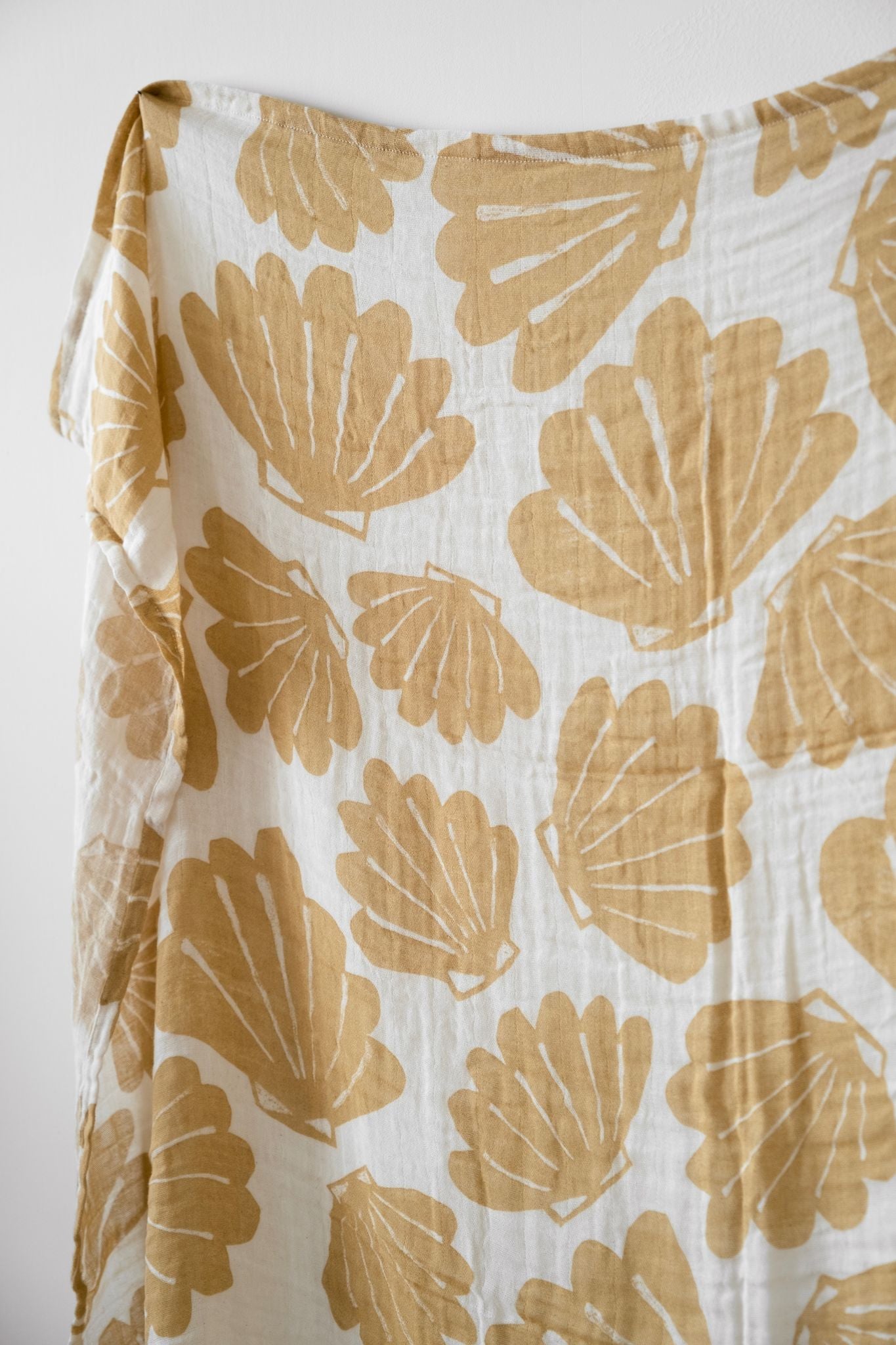 An outstretched muslin blanket with a shell pattern in an off-white/sand colour.