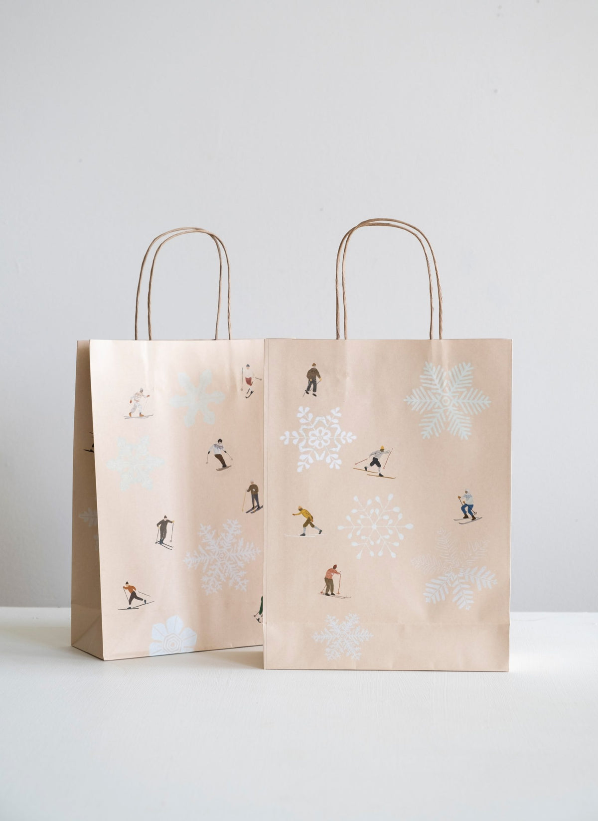 Two beige paper bags with winter-themed illustrations on a light gray background.