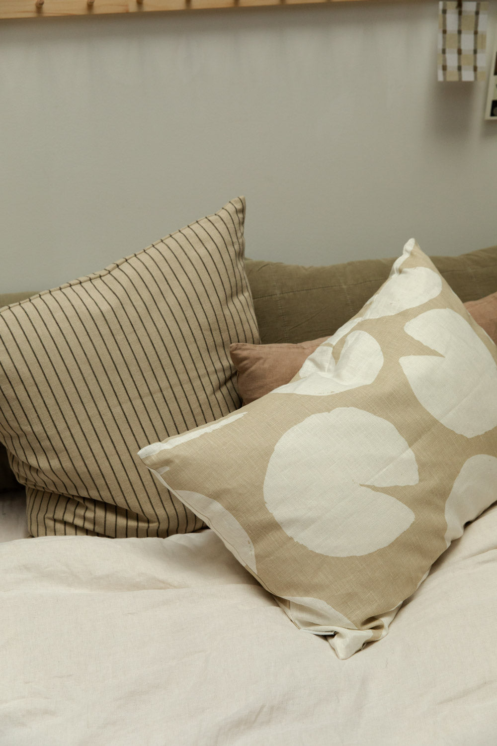 Fine Little Day Water Lilies sand cushion, Kare striped cushion against a eucalyptus linen headboard cushion on a bed.