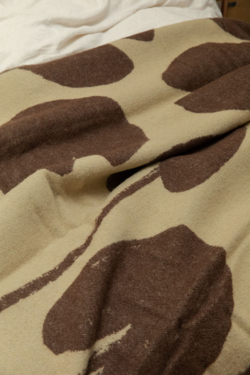 Close-up of Fine Little Day Water Lilies wool blanket in sand and chocolate brown showing large bold floral print and soft texture detail draped across a bed.