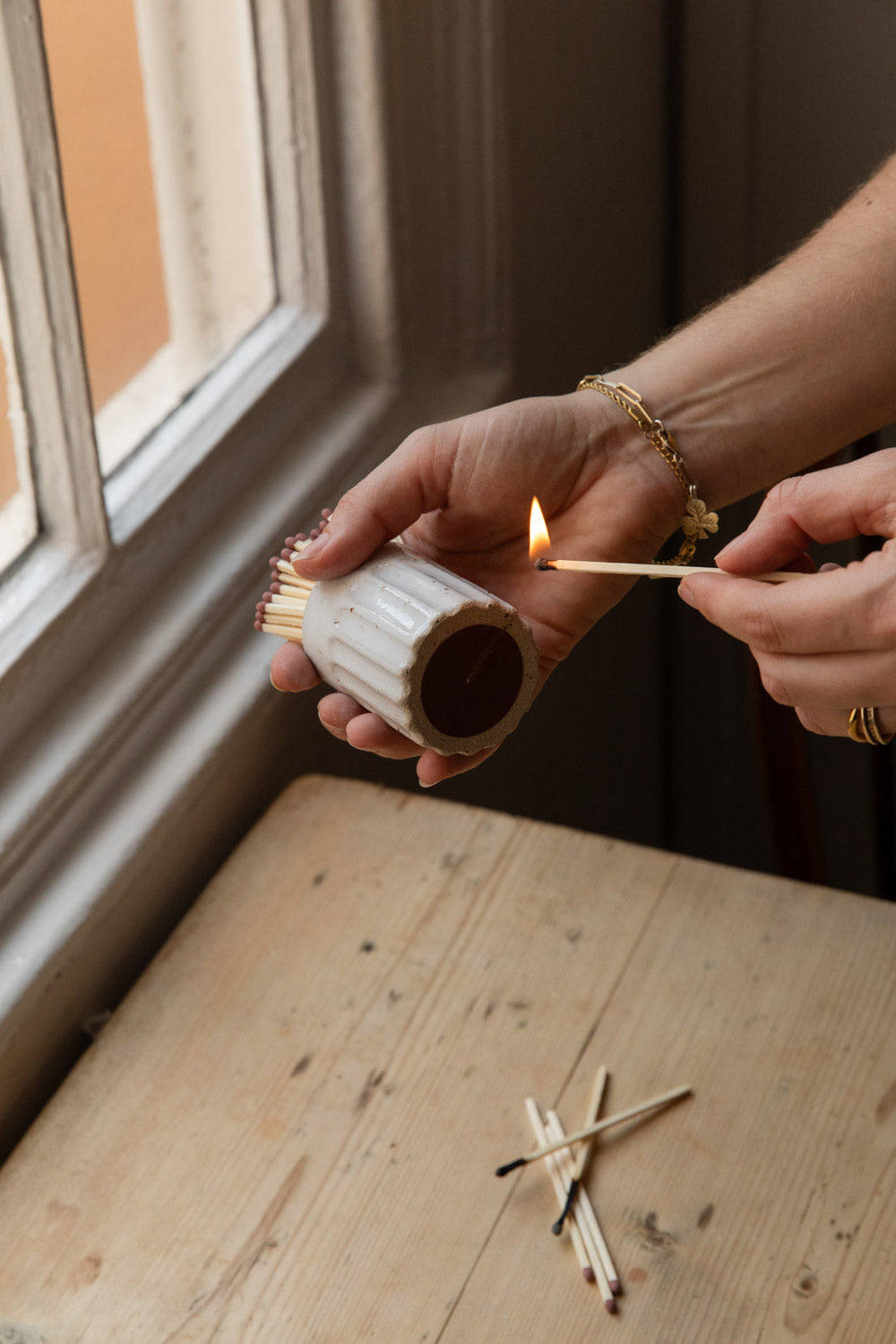Striking an extra long match on the base of a white speckled fluted match pot