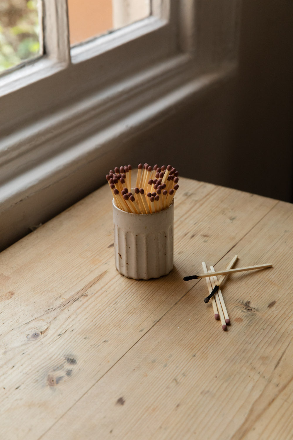 White speckled fluted stoneware match pot full of extra long matches on a table by the window