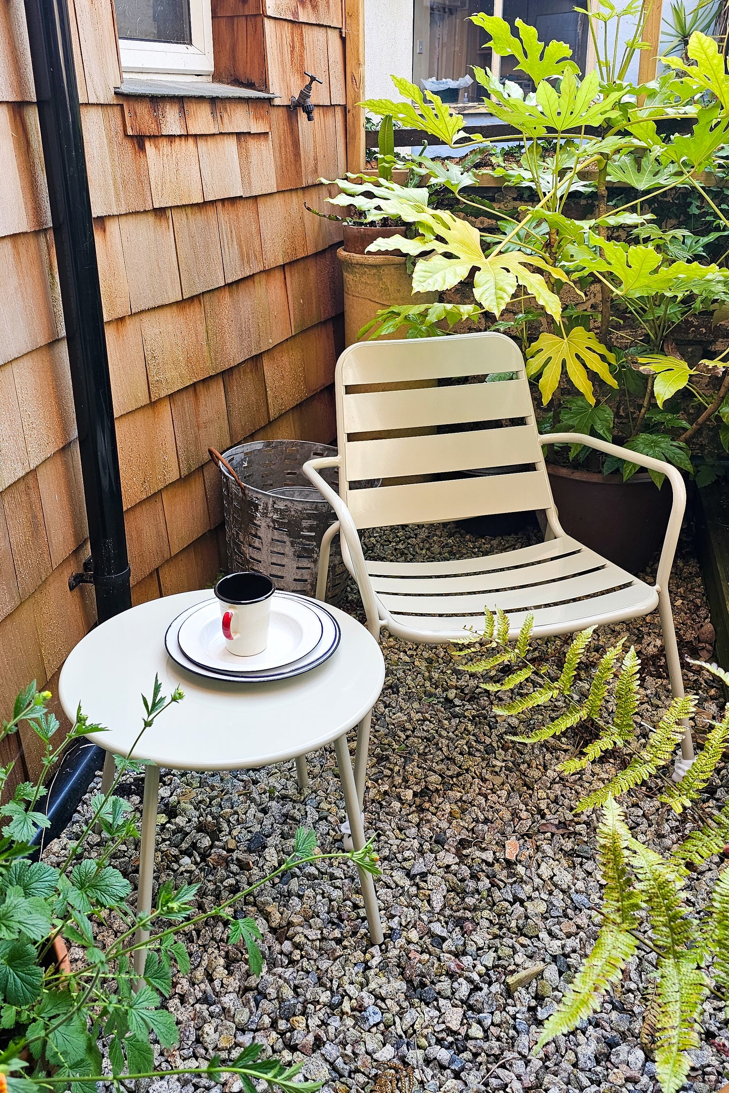 A garden with a clay coloured outdoor armchair and matching table. 