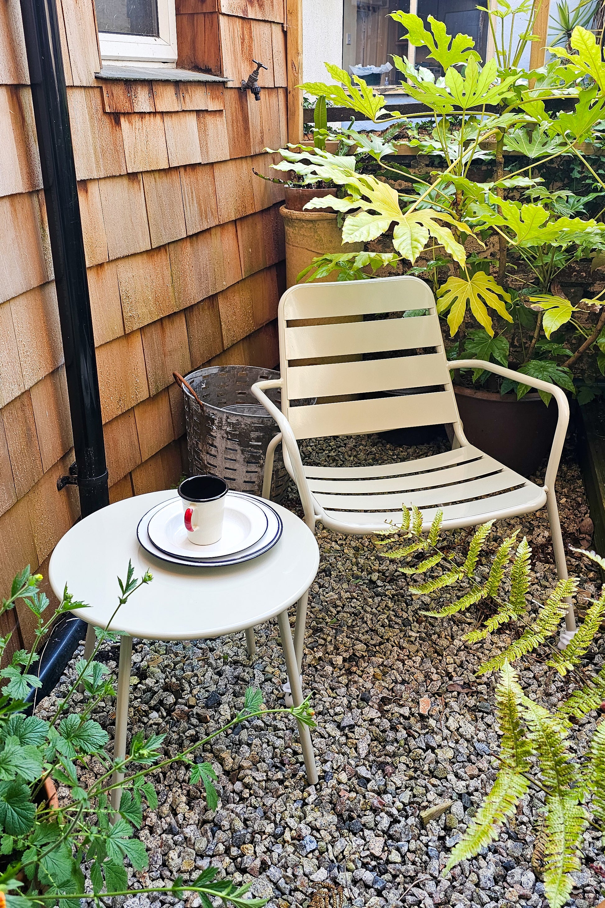 A garden with a clay coloured outdoor armchair and matching table. 