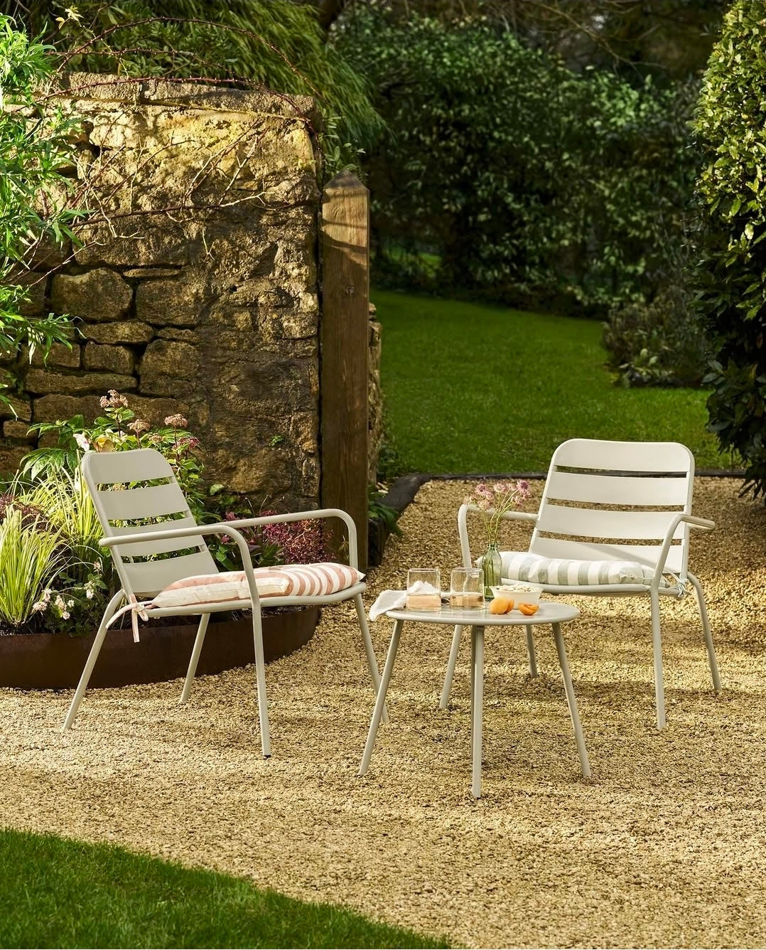 A garden with two clay coloured armchairs and matching table.