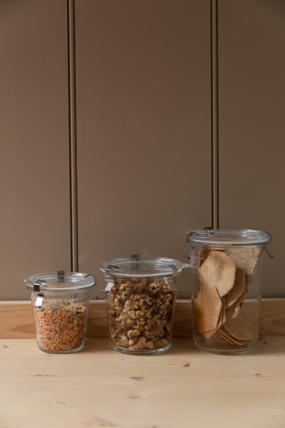 Three glass storage jars with metal clips holding lentils, walnuts and crispbreads