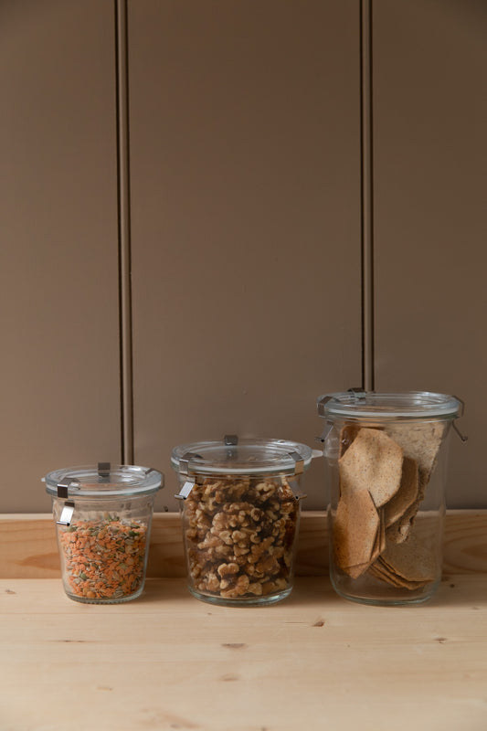 Three glass storage jars with metal clips holding lentils, walnuts and crispbreads