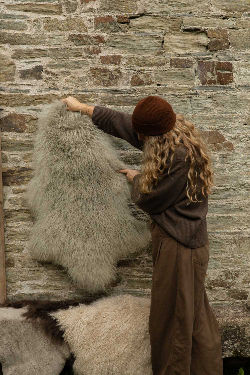 Silvery grey Tibetan sheepskin rug with soft curls held up against a Cornish stone wall