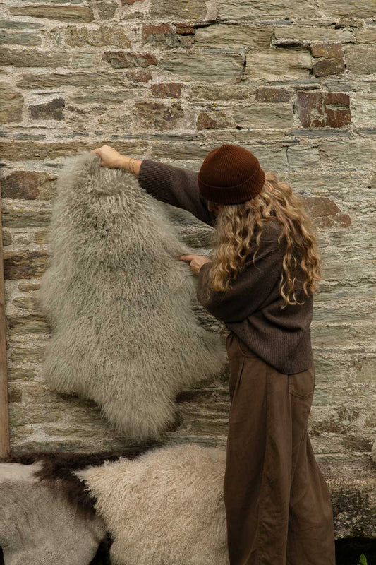 Silvery grey Tibetan sheepskin rug with soft curls held up against a Cornish stone wall
