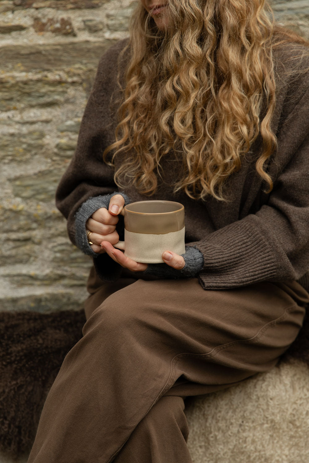Half glazed stoneware mug in truffle brown held in both hands against a cosy knit
