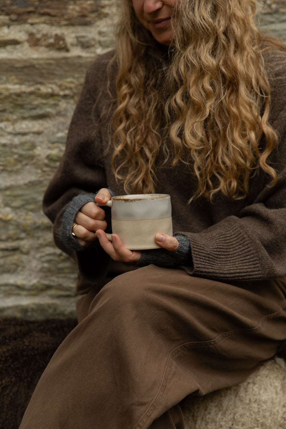 Half glazed stoneware mug in white held in both hands, the raw clay base showing below the glaze