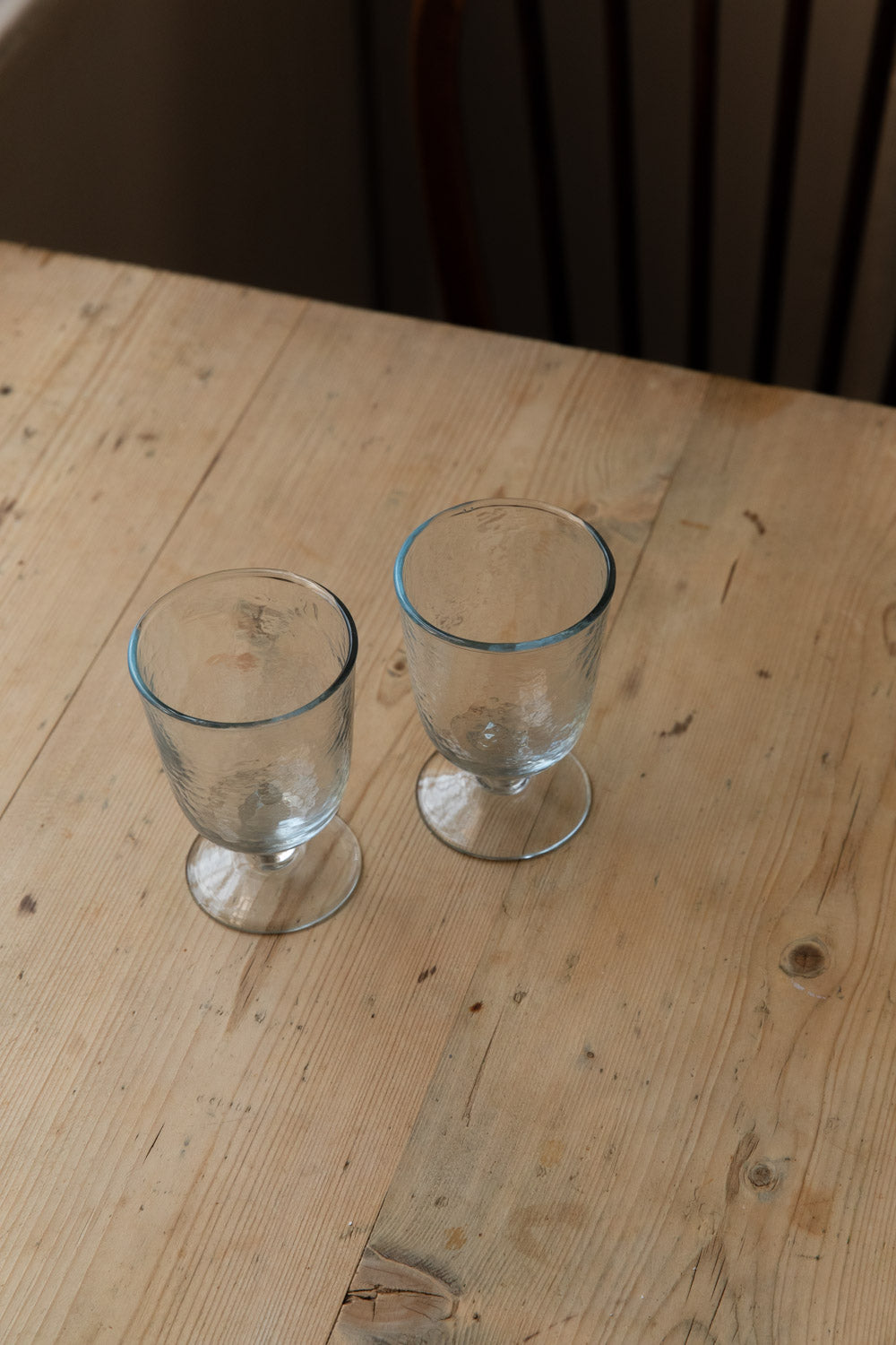 Pair of hammered goblet glasses with short stems on a pine kitchen table