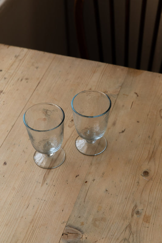 Pair of hammered goblet glasses with short stems on a pine kitchen table
