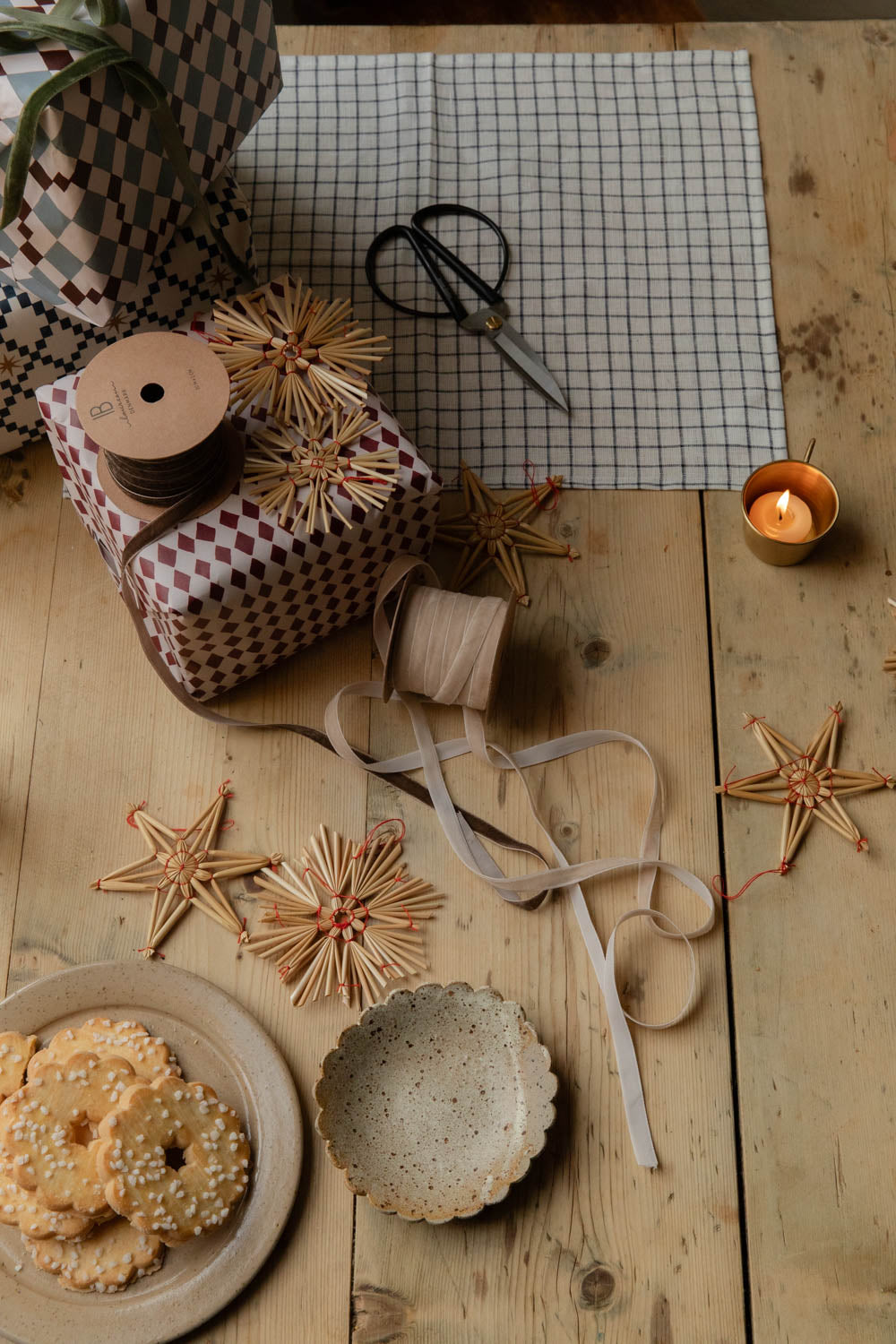 Gift wrapping table with harlequin paper, ribbon spools, straw stars and biscuits