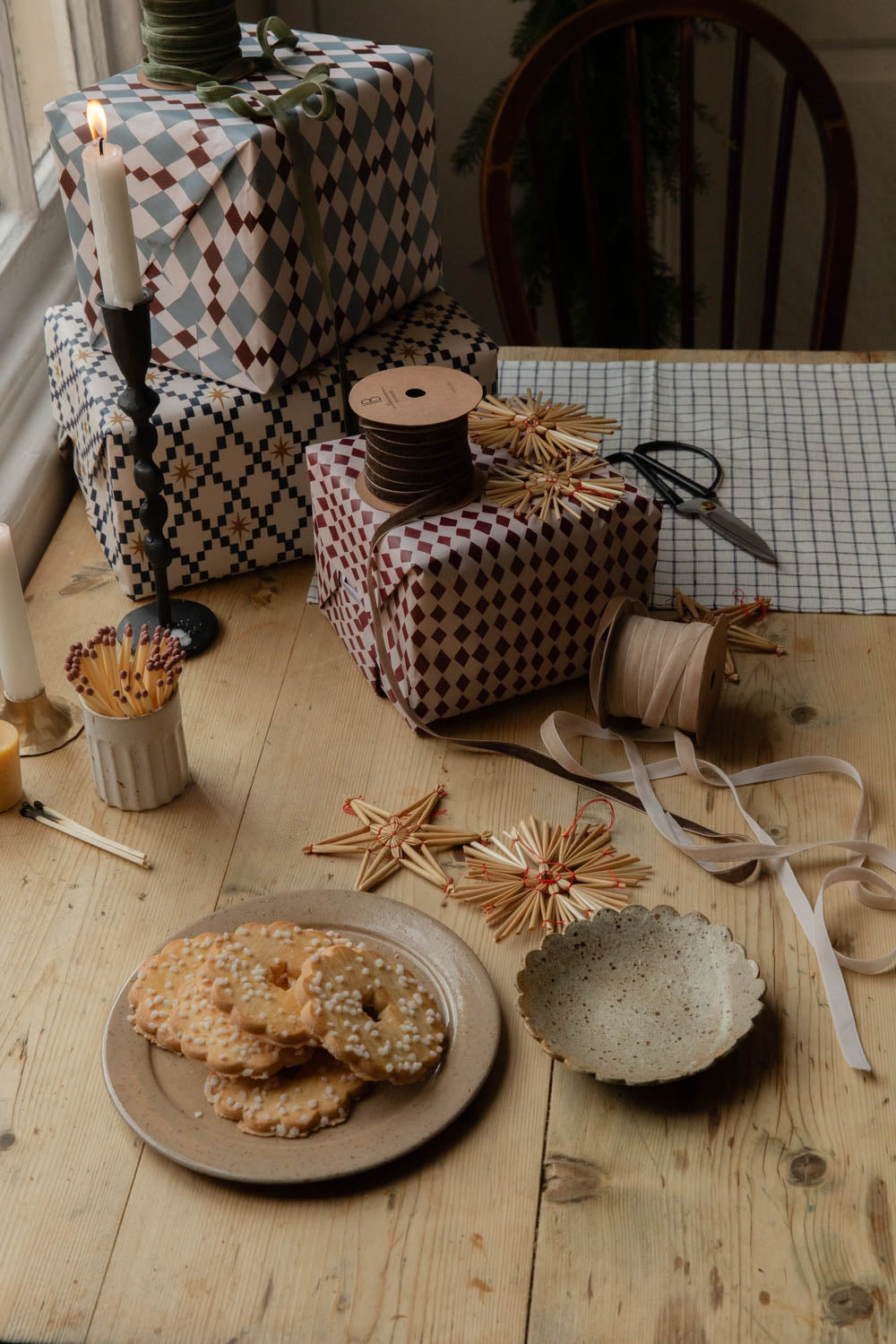 Stack of harlequin wrapped presents with ribbon, matches and straw stars on a table