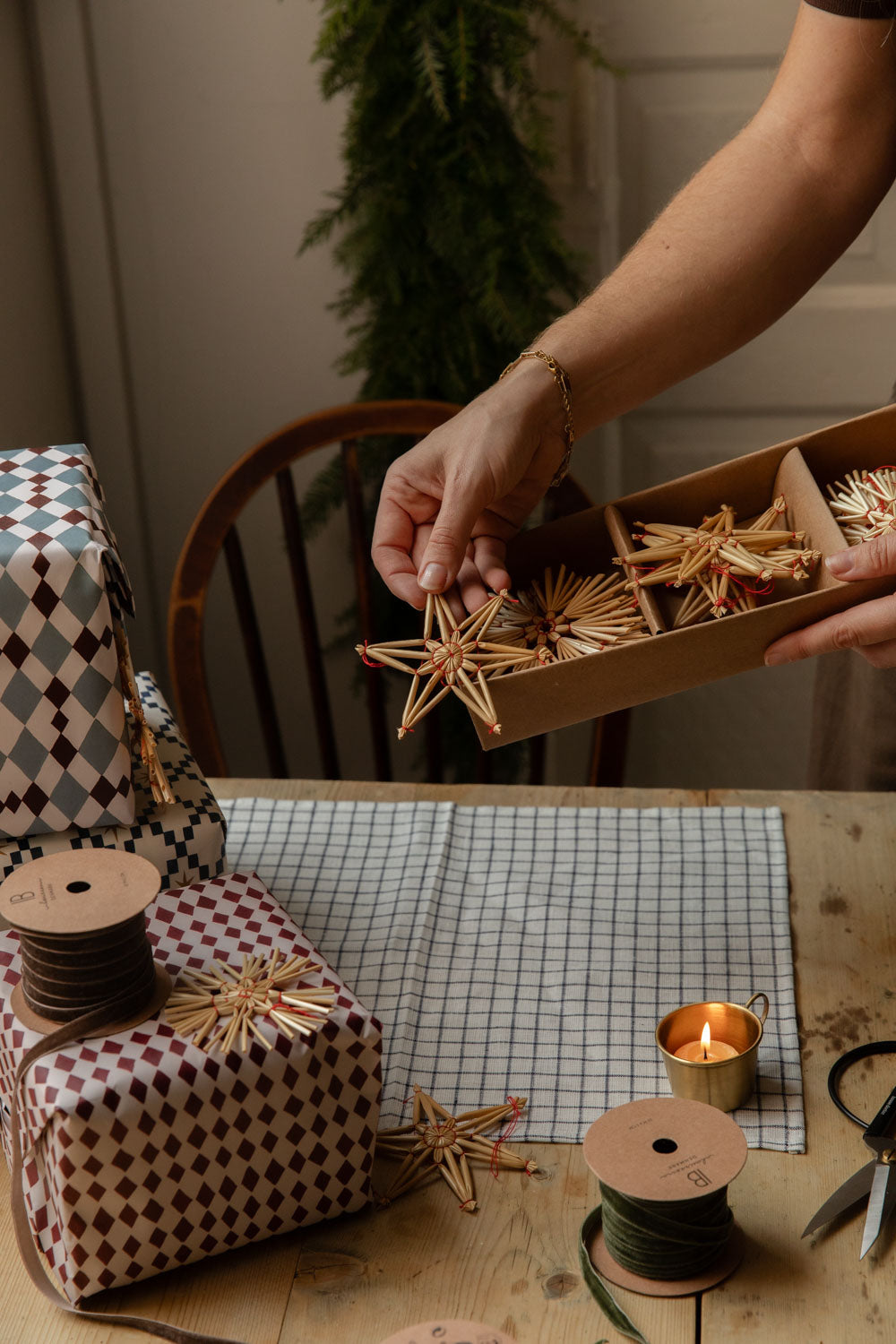 Hand lifting straw stars from a box beside parcels in harlequin gift wrap