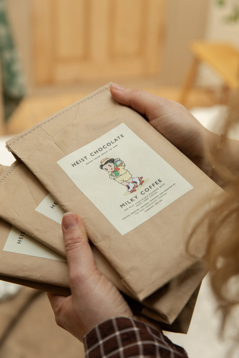 Hands holding a stack of Heist Chocolate Milky Coffee bars in kraft paper packaging.