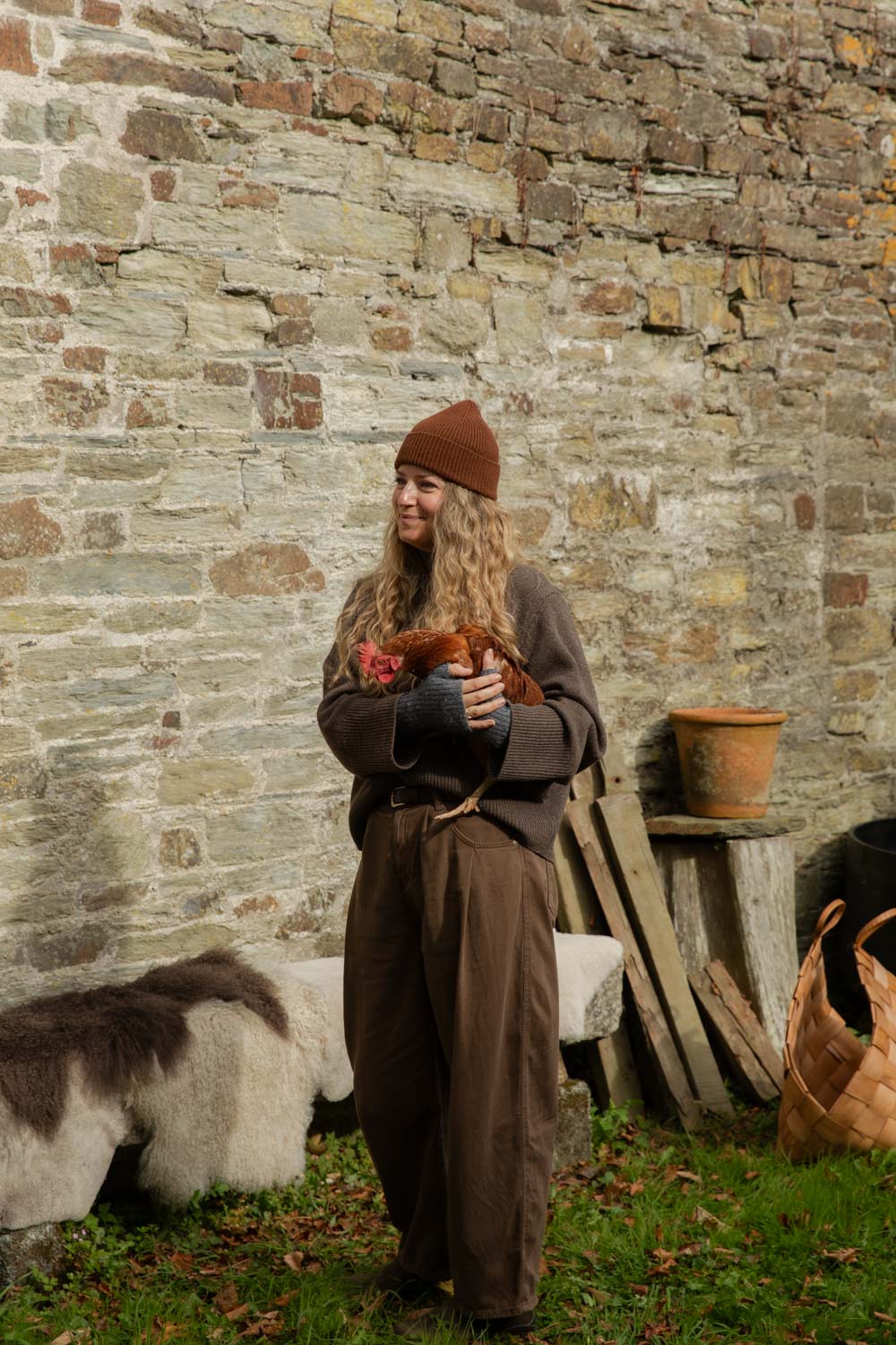 Woman in a brown ribbed beanie holding a hen in a cottage garden