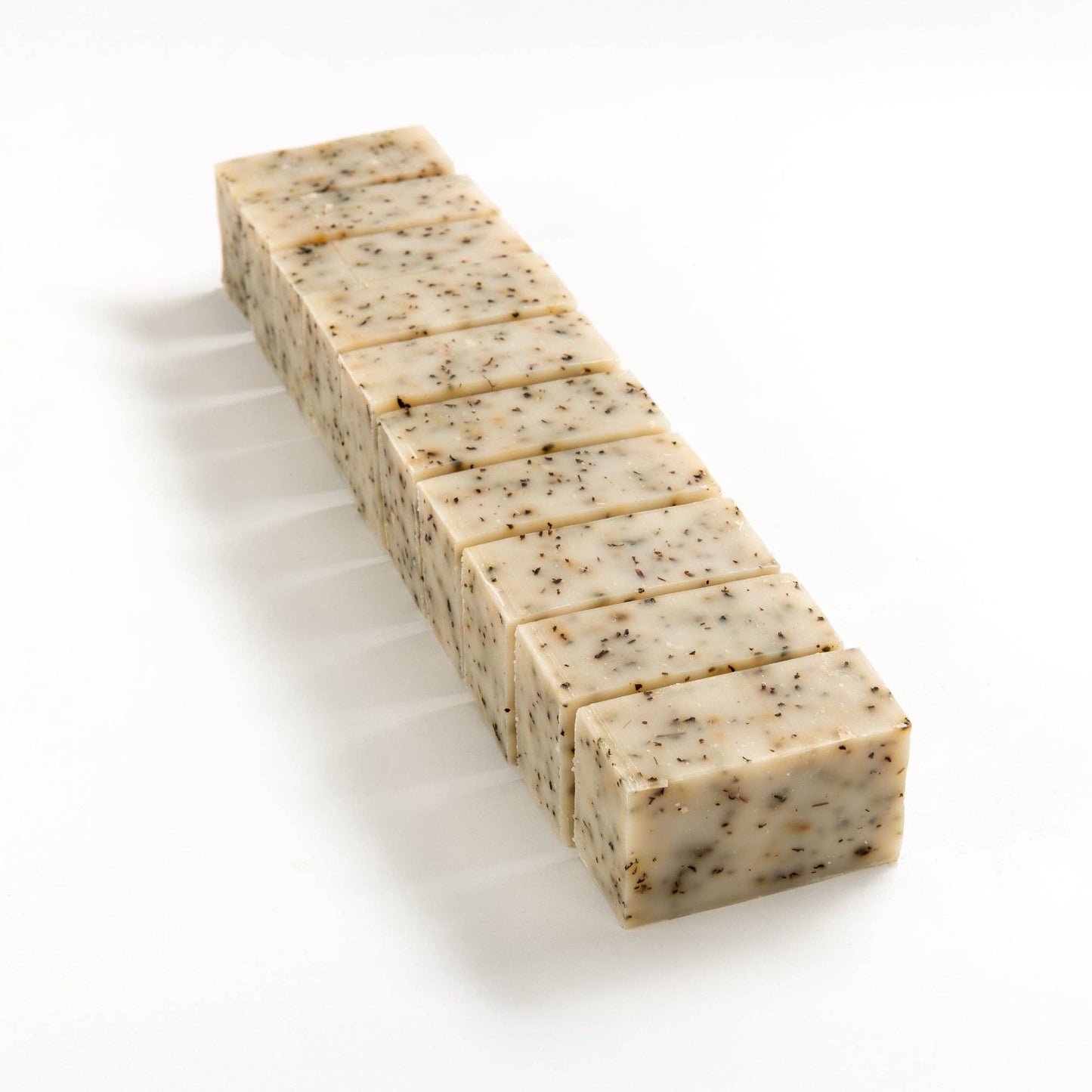 Row of herbal mint soap brick cut into smaller pieces on a white background.
