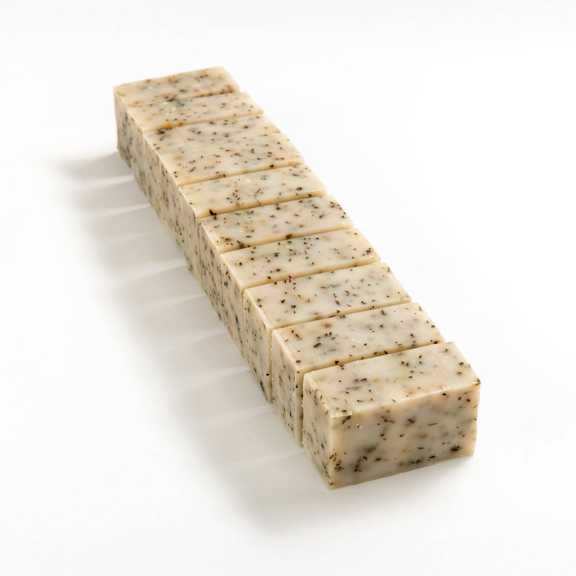 Row of herbal mint soap brick cut into smaller pieces on a white background.