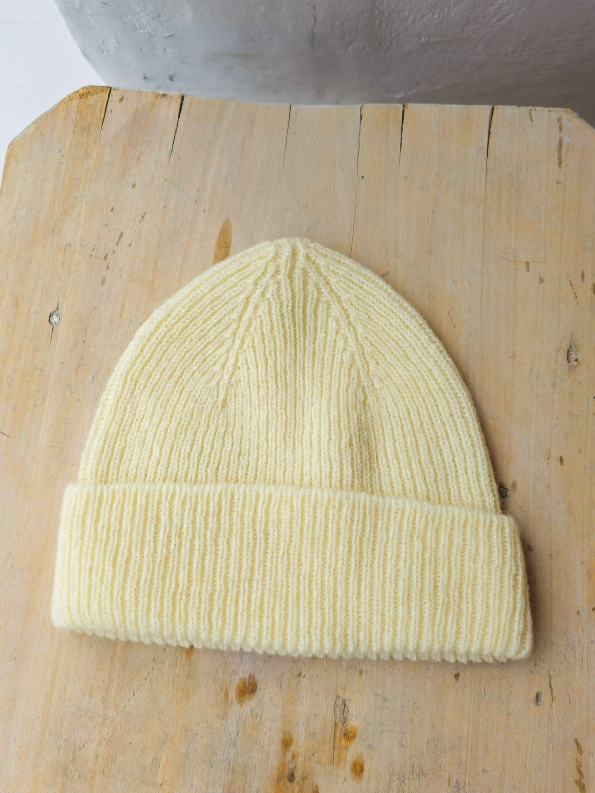 A pale ecru ribbed knit beanie hat resting on a light wood surface.