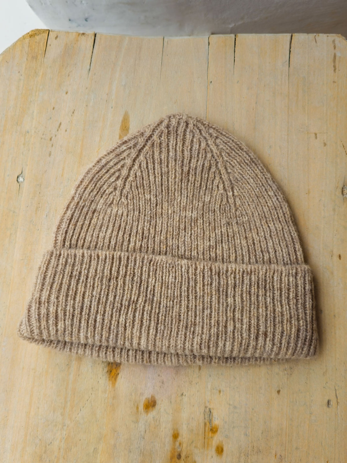 A beige ribbed knit beanie hat resting on a light wood surface.