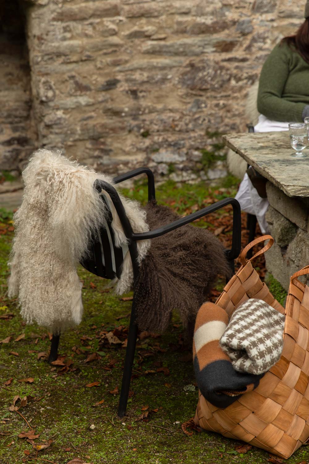 Cream and brown Tibetan sheepskins over a black garden chair, beside a woven basket holding a houndstooth wool blanket