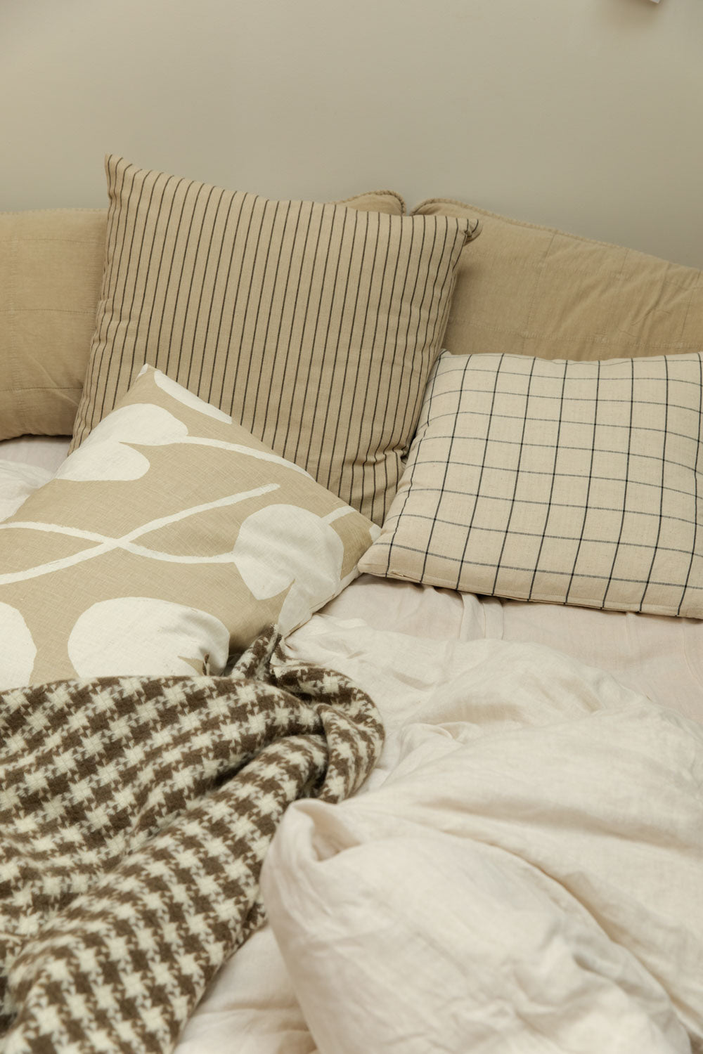 Layered bed styling with houndstooth wool throw, stripe and grid linen cushions and large abstract print cushion.