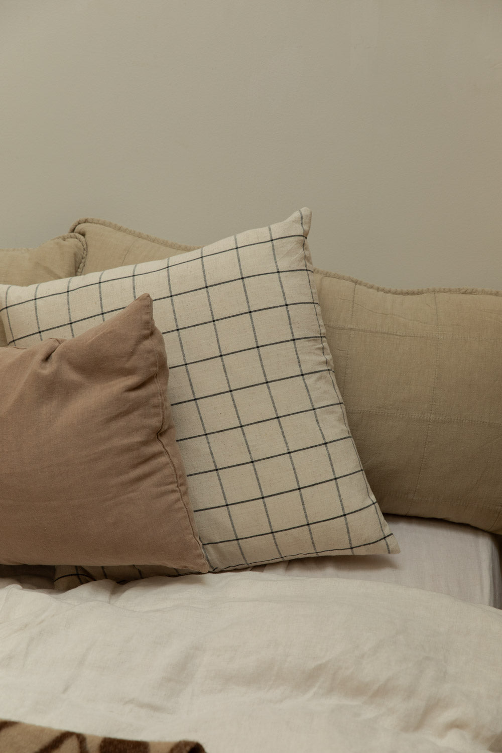 House Doctor Join grid check linen cushion cover propped against a quilted linen headboard cushion on a white linen bed.