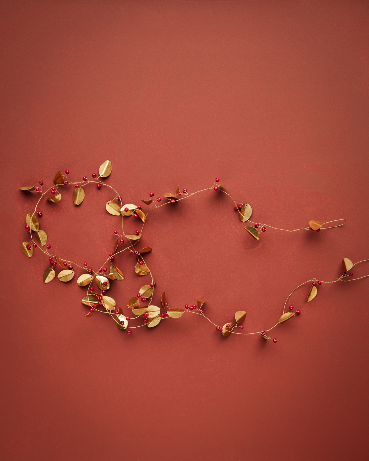 Brass coloured metal and red wooden bead garland on an orangey red background.